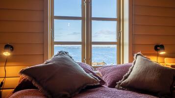 A bed with a view of the sea through a window, two bedside lamps, and a textured blanket.