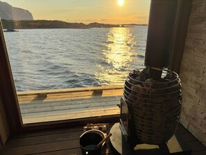A wood stove on a deck with a view of the water and a sunset.