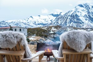 Two chairs facing a wood-burning stove with a mountain backdrop.