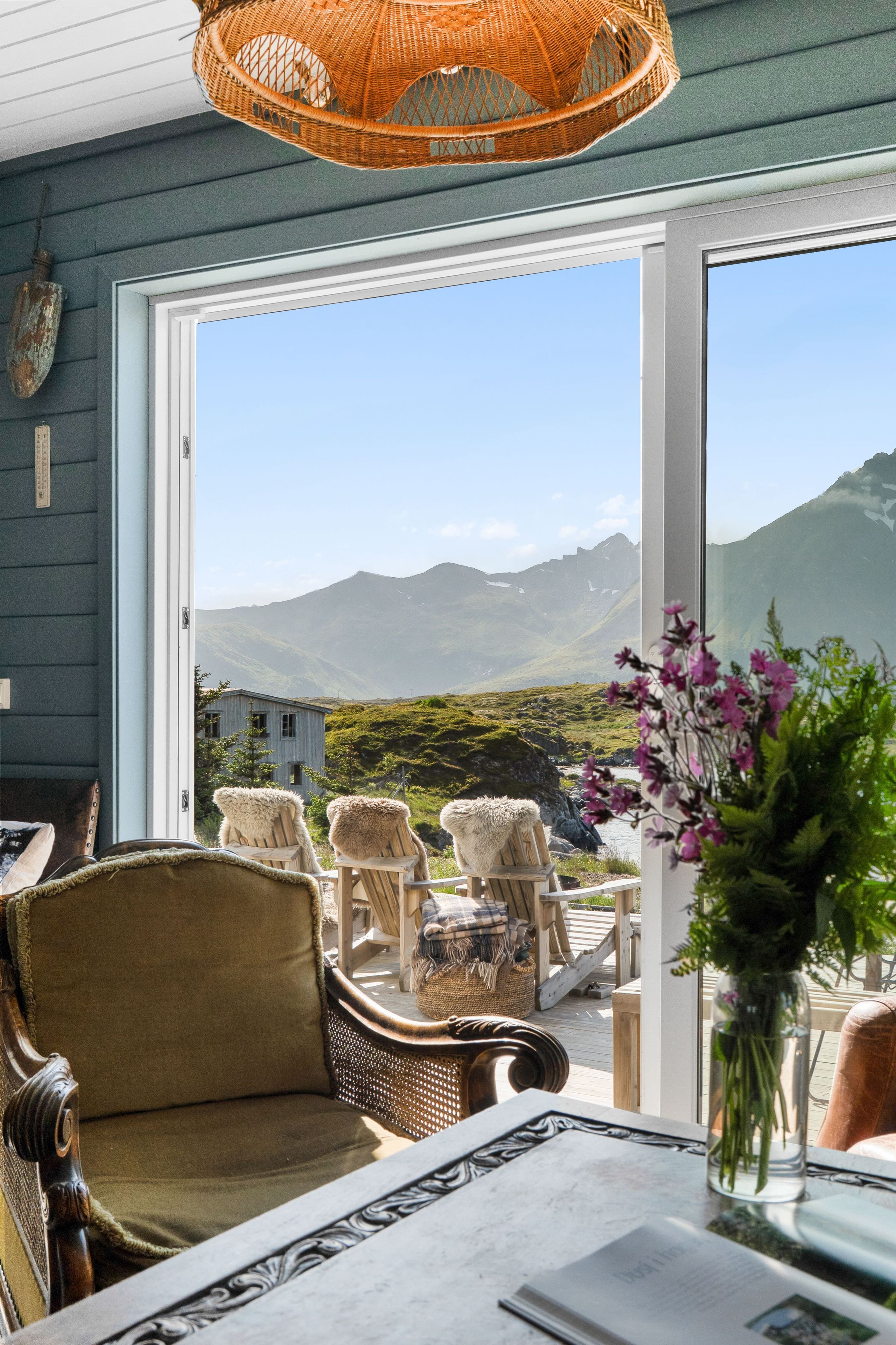 Et værelse med udsigt til bjerge, fletmøbler og et bord med en vase blomster.