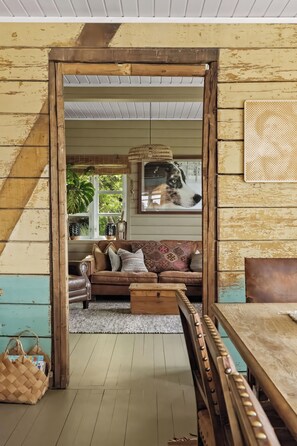 A rustic interior with a wooden-framed doorway leading to a living area featuring a brown sofa, patterned cushions, and a woven basket.