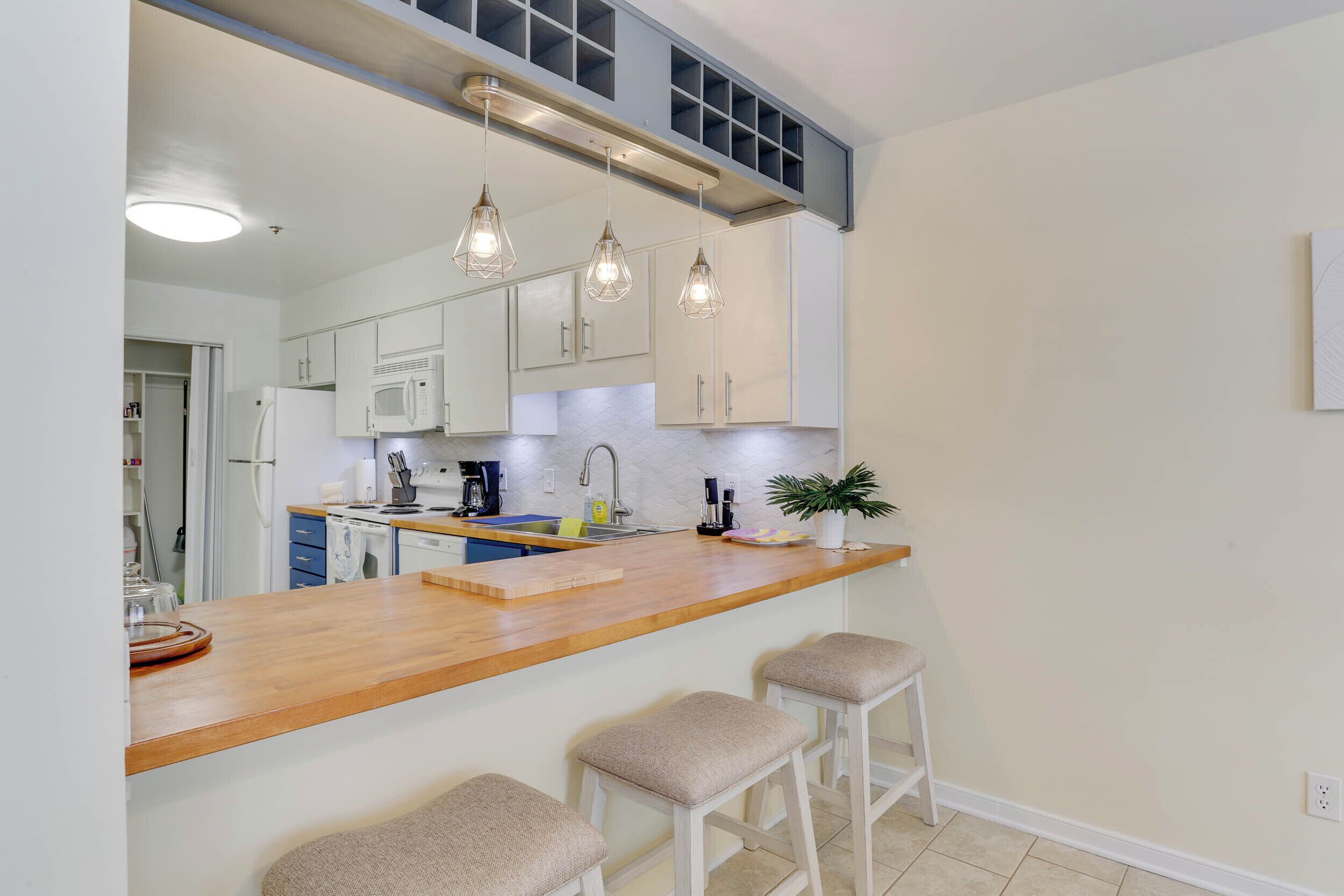 A modern kitchen with white cabinets, a wooden countertop, and three bar stools.