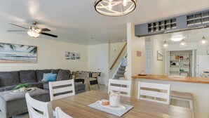 Un salon moderne avec une table à manger, des chaises blanches, un canapé gris et un ventilateur de plafond.