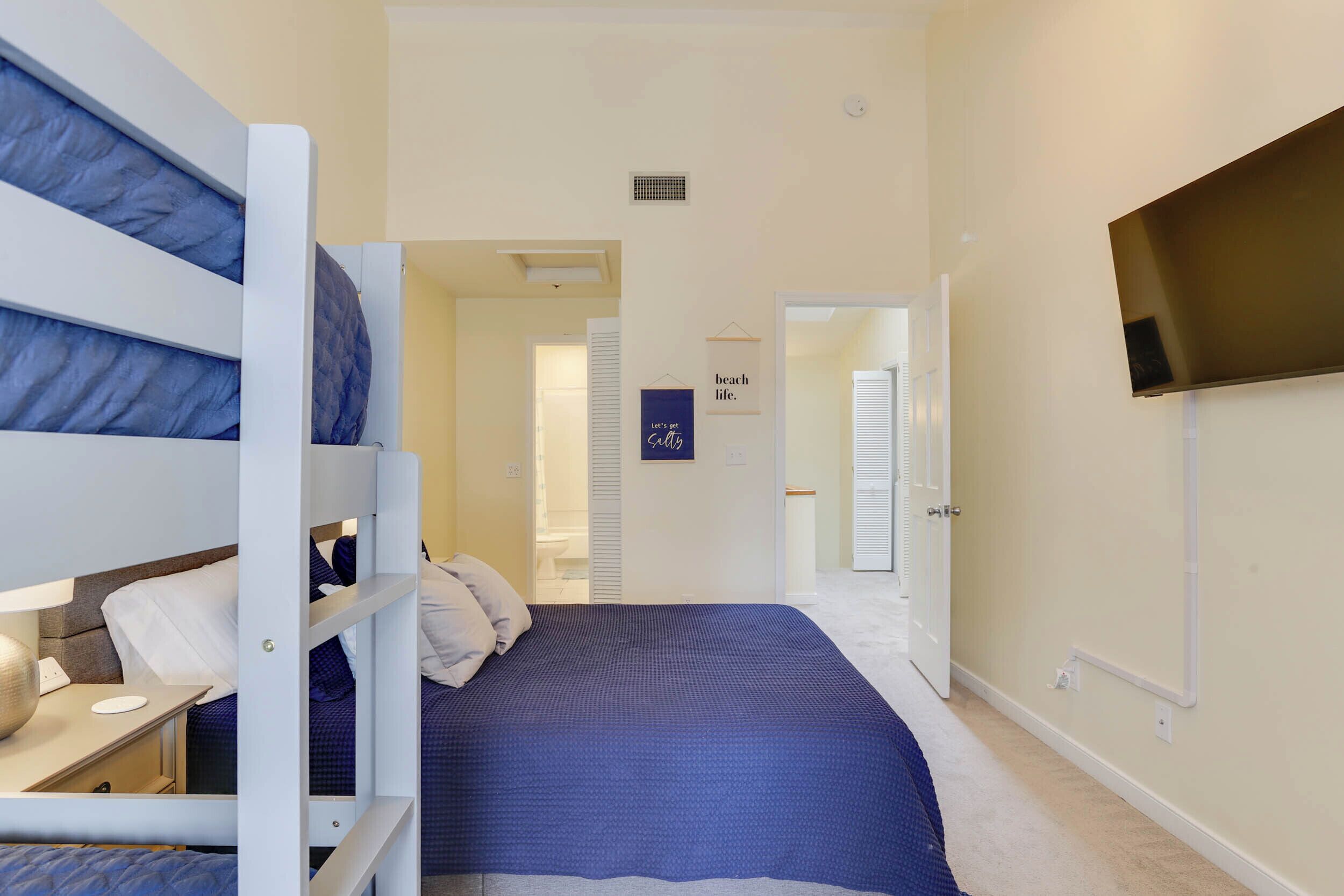 A bedroom with bunk beds, a flat-screen TV, and a bed with a blue bedspread.