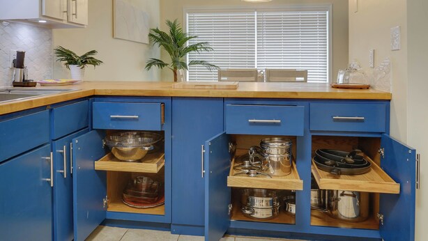 Une cuisine avec des armoires bleues, des plans de travail en bois et des étagères intégrées pour ranger les ustensiles de cuisine.