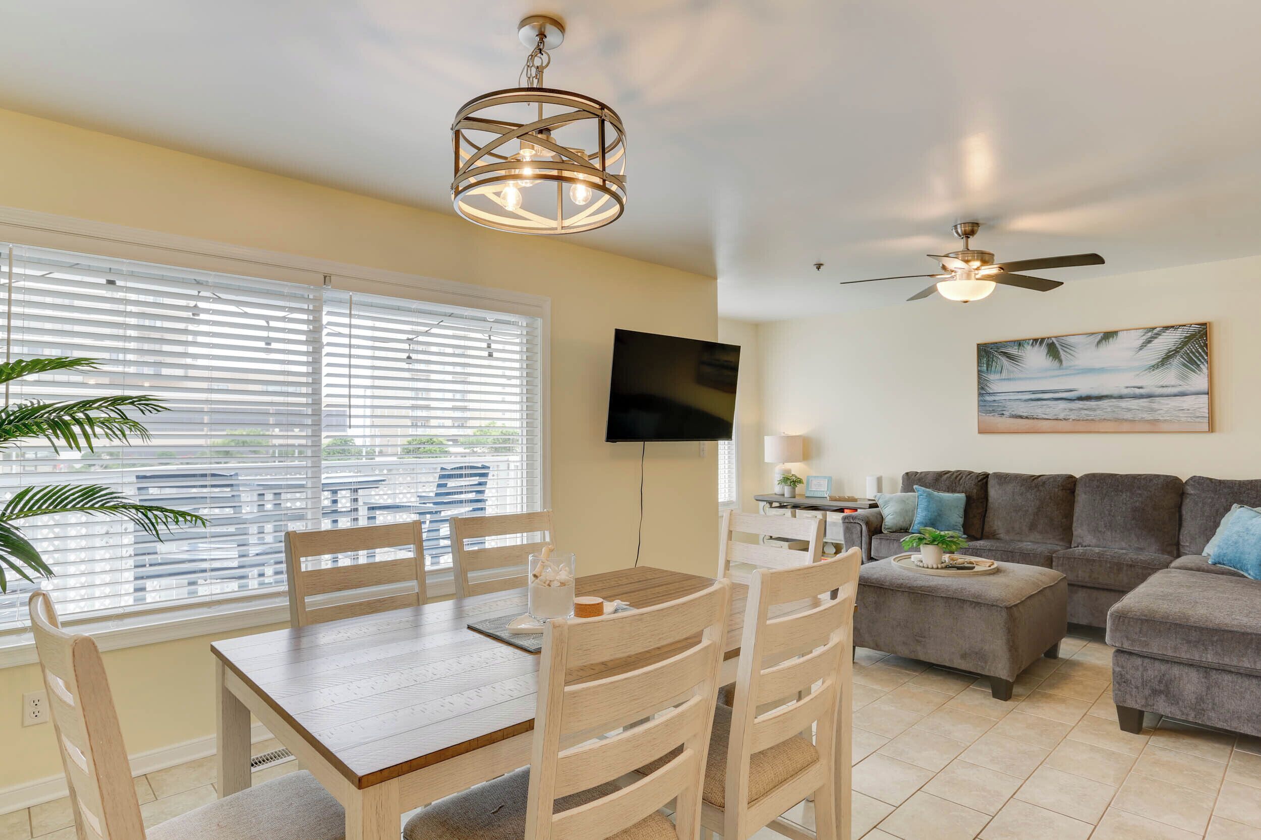 Un salon comprenant une table à manger, des chaises, un canapé, un ventilateur de plafond et un téléviseur fixé au mur.