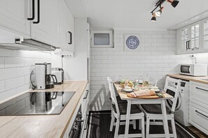 Une cuisine compacte avec des meubles blancs, un four encastré, une machine à café et une table à manger pour deux personnes.