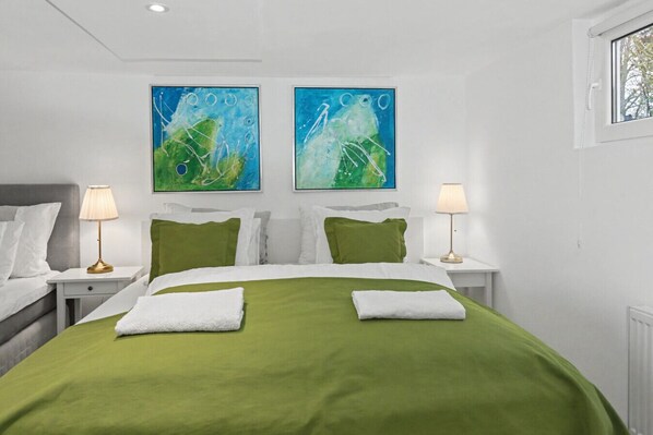 Une chambre d’hôtel moderne avec une couvre-lit verte, du linge de lit blanc et deux tableaux abstraits au-dessus du lit.