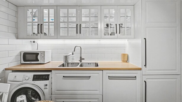 Une cuisine moderne avec des meubles blancs, un four à micro-ondes, un évier et un lave-linge.