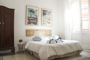 Ein Schlafzimmer mit Bett, Holz-Kopfteil, Nachttisch, kleiner Topfpflanze und zwei gerahmten Bildern an der Wand.