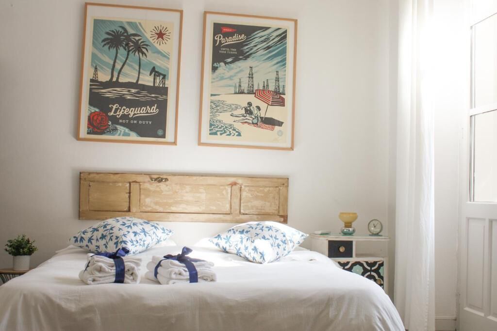Un lit bien fait, avec des serviettes et un oreiller bleu, une tête de lit en bois et deux affiches encadrées au mur.