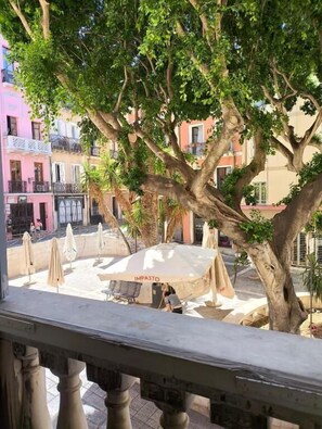A tree-lined outdoor seating area with umbrellas and a bench, overlooking a street with colorful buildings. - Sa Prazza Guesthouse (Cagliari)