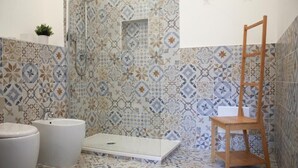 Une salle de bain avec des carreaux décorés, une douche, un lavabo et une chaise en bois.