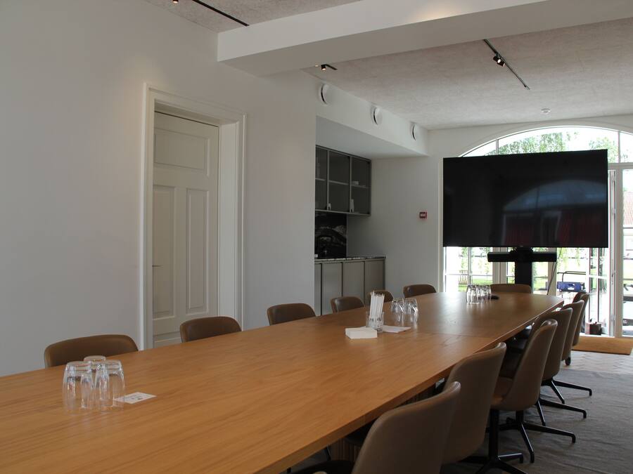 A conference room with a long table, chairs, a flat-screen TV, and a door.