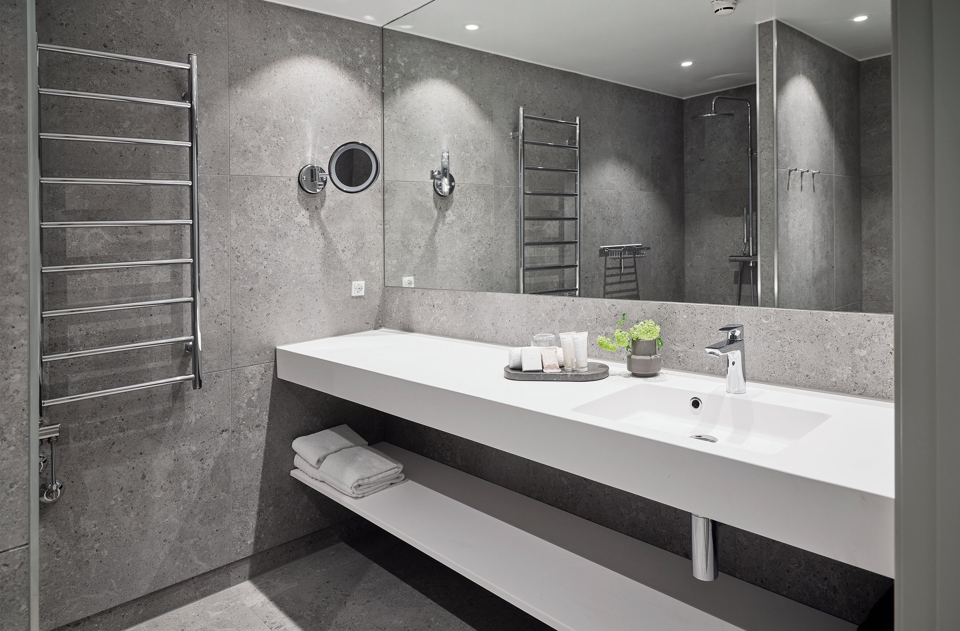 Un baño moderno con un espejo grande, dos lavamanos, un perchero para toallas y una zona de ducha.