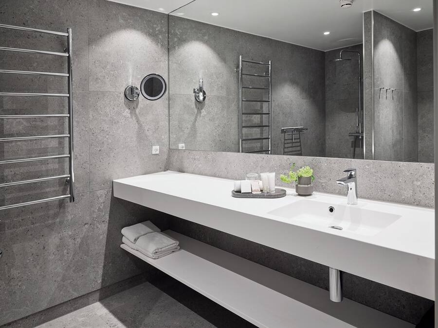 A modern bathroom with a large mirror, two sinks, a towel rack, and a shower area.