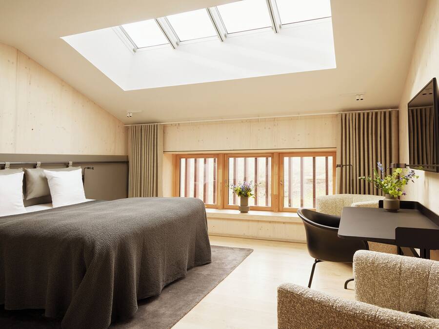 A bedroom with a skylight, a bed, a desk, and a chair.