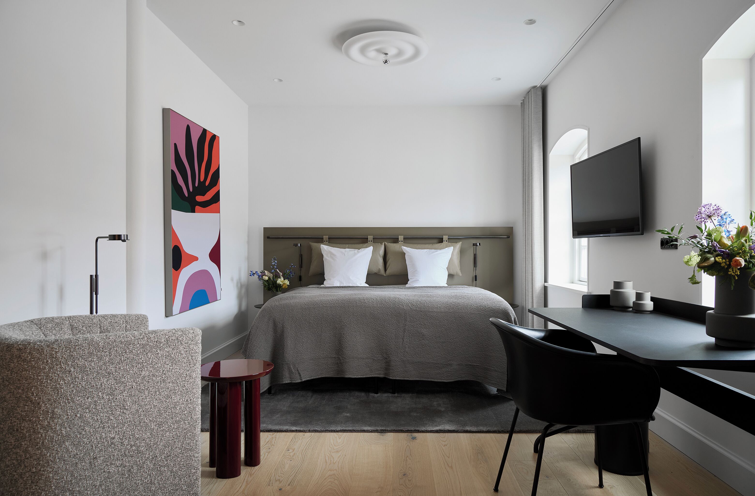 Un dormitorio moderno con una cama, un escritorio, una silla, un televisor y un cuadro abstracto grande.