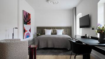 A modern bedroom with a bed, a desk, a chair, a TV, and a large abstract painting.