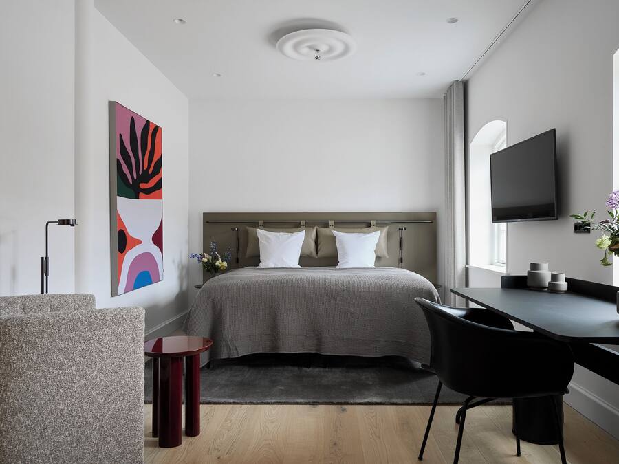 A modern bedroom with a bed, a desk, a chair, a TV, and a large abstract painting.