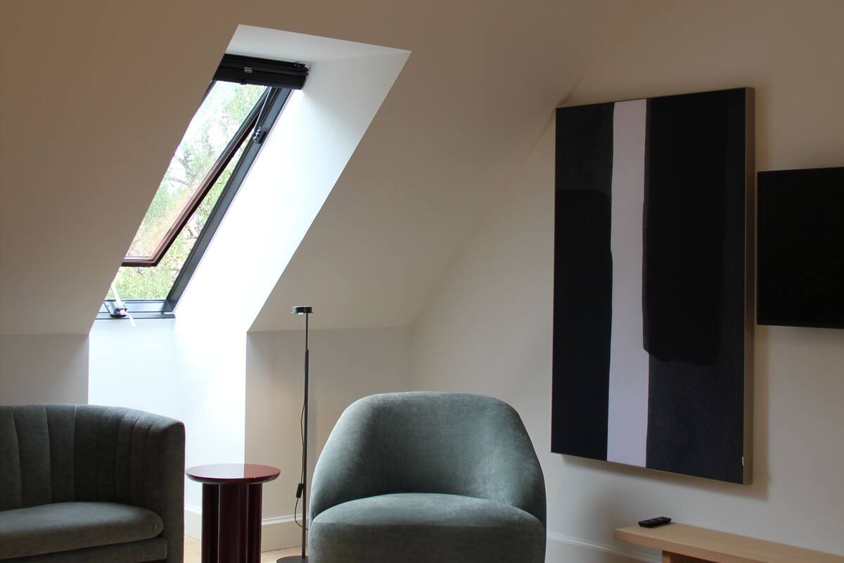 Una camera moderna con soffitto spiovente, una grande finestra, un divano, una panca e un quadro appeso al muro.