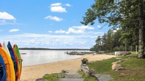 En vacker utsikt över sjön med kajaker, en sandstrand och en stenlagd gångväg som leder till en brygga.