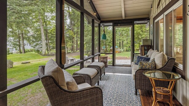 En inglasad veranda med möbler i rotting, ett glasbord och utsikt över ett grönskande landskap.