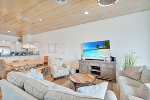 A modern living room with a wooden ceiling, a flat-screen TV, a sofa, a coffee table, and a dining area with a wooden table and chairs. - Marina front condo with a rooftop deck and a hot tub! (Port Aransas)