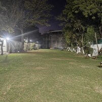 A nighttime outdoor area with a grassy lawn, trees, and a building with a concrete facade.