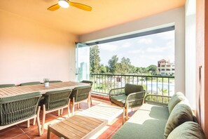 Un balcon avec une table et des chaises en bois, un canapé et une vue sur un immeuble et des arbres.