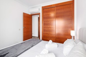 Une chambre d’hôtel avec un lit, un tapis de couleur grise, une armoire en bois et une table de chevet avec une lampe.