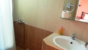Um banheiro com vaso sanitário branco, chuveiro com banheira envidraçada, pia bege com espelho acima e tapete listrado vermelho no chão.