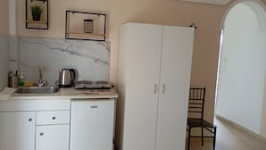 Cozinha com pia, fogão e armários. Há uma cadeira e uma porta que dá para outro cômodo.