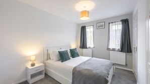 Un dormitorio con cama, mesita de noche, lámpara de noche y ventana con cortinas.