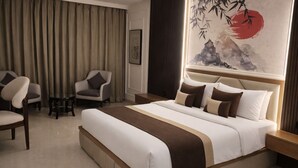 Une chambre d’hôtel avec un grand lit, deux fauteuils, une petite table et un tableau au mur.