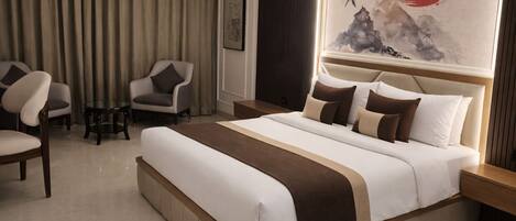 Une chambre d’hôtel avec un grand lit, deux fauteuils, une petite table et un tableau au mur.