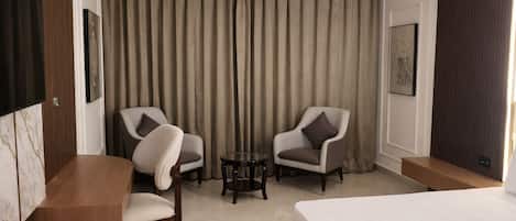 A hotel room with a bed, two armchairs, a small table, and a large window with curtains.