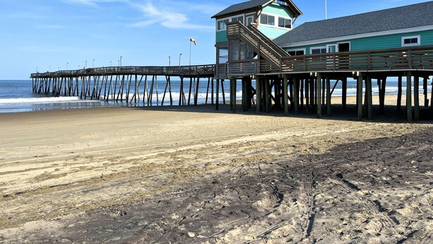 Un muelle de madera que se extiende hacia el océano, con un edificio que tiene una torre y un balcón.