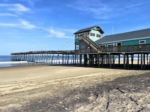 A wooden pier extending into the ocean with a building featuring a tower and a balcony.