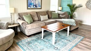 Una sala de estar con un sofá color beige, una mesa de centro de madera, un tapete azul estampado y un ventilador de techo.