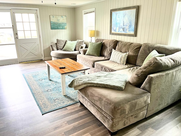 A living room with a brown sectional sofa, a wooden coffee table, and a blue patterned rug.
