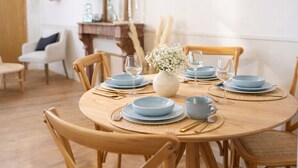 Een eethoek met een ronde houten tafel voor vier personen, omringd door houten stoelen met geweven zittingen.