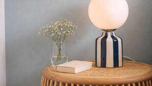 Een ronde houten tafel met een witte lamp en een bloemenvaas.
