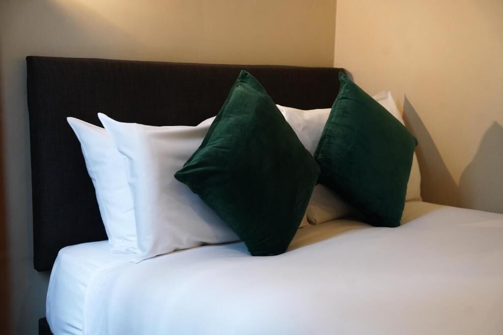 A bed with white and green pillows, a dark headboard, and a plain wall.