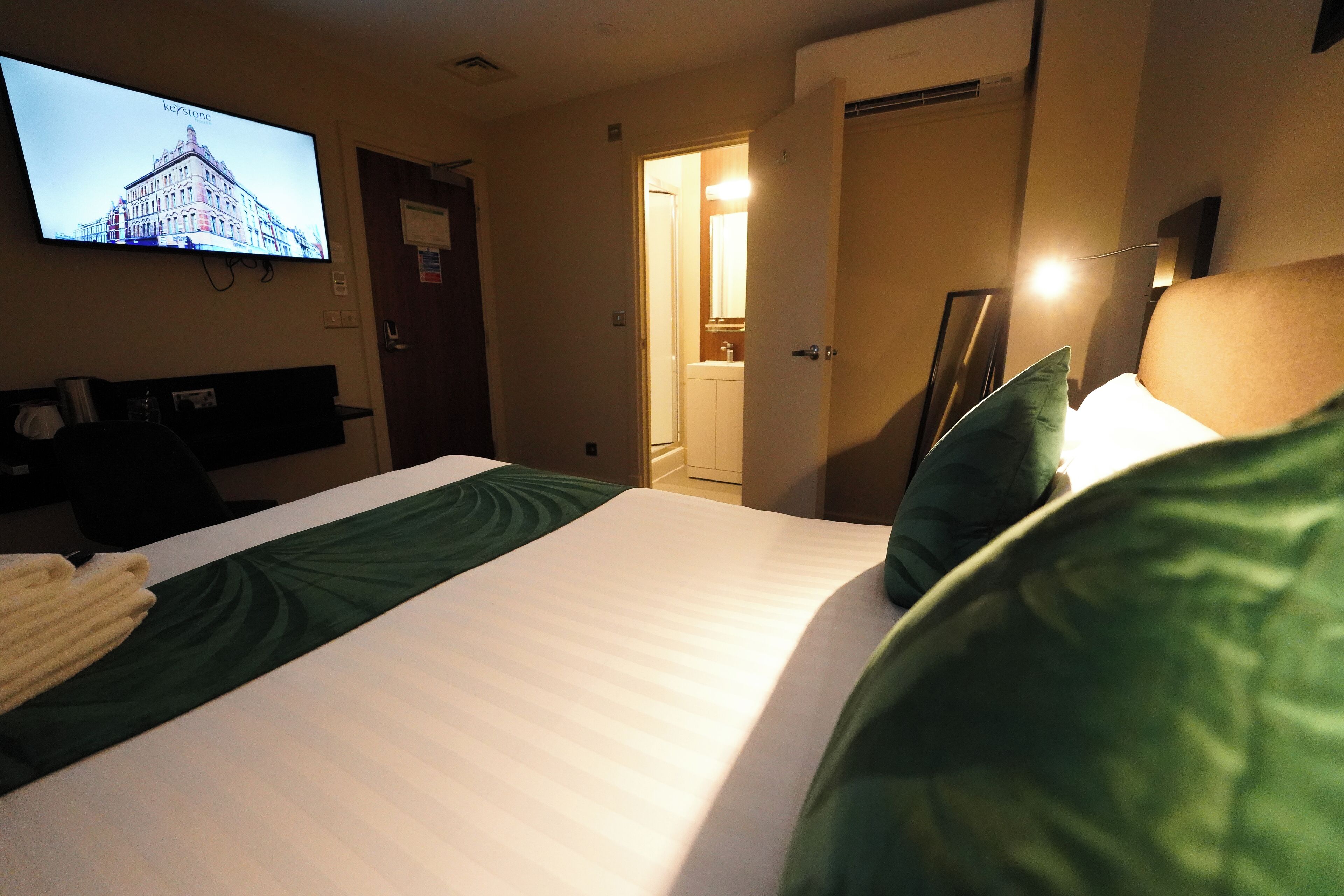 A hotel room with a bed, a television mounted on the wall, and a bathroom visible through an open door.
