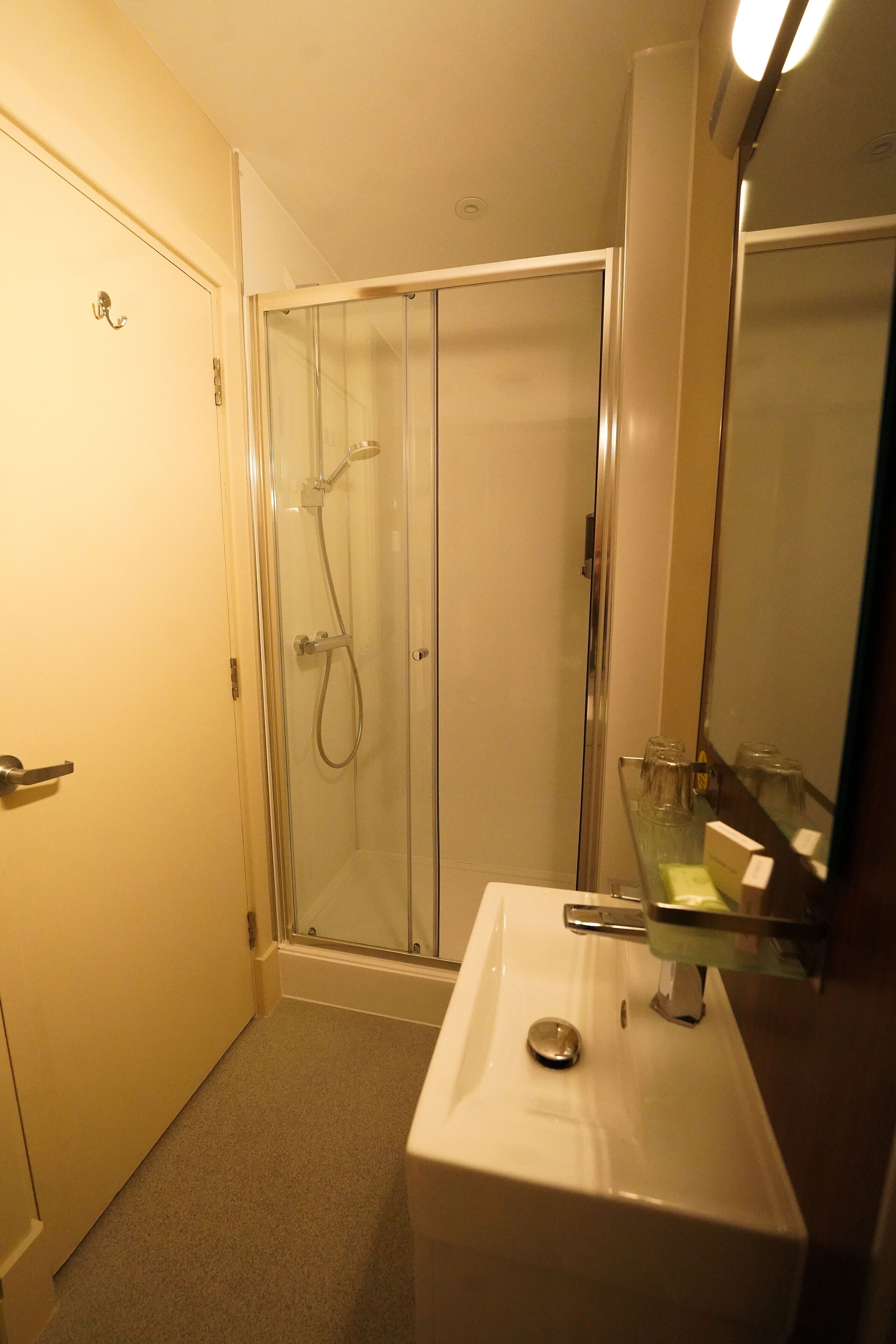 Un baño con cabina de ducha de vidrio, un lavabo blanco y un espejo.
