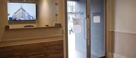 A hotel entrance with a glass door, a reception desk, and a digital screen displaying a building image.
