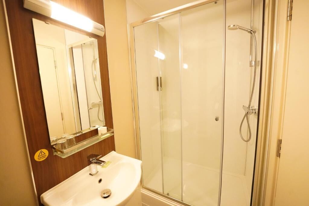 Un baño con cabina de ducha de vidrio, un lavabo con espejo y un estante con artículos de tocador.