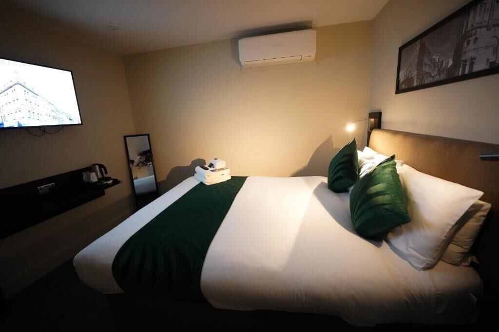 Une chambre d’hôtel équipée d’un lit, d’un téléviseur à écran plat fixé au mur, d’un climatiseur et d’un tableau encadré accroché au mur.