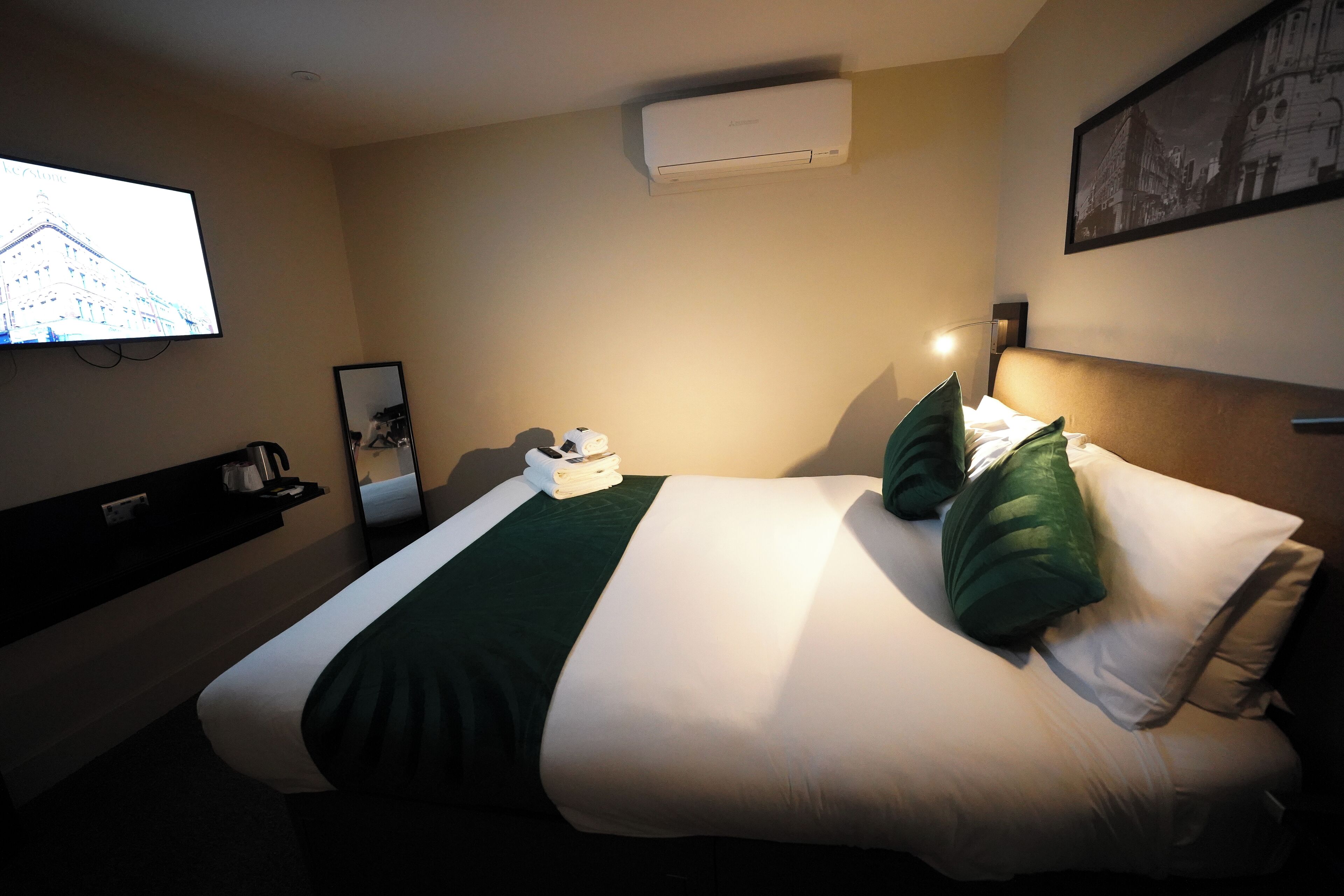 Quarto de hotel com uma cama, uma televisão fixada na parede, aparelho de ar condicionado e um quadro pendurado na parede.